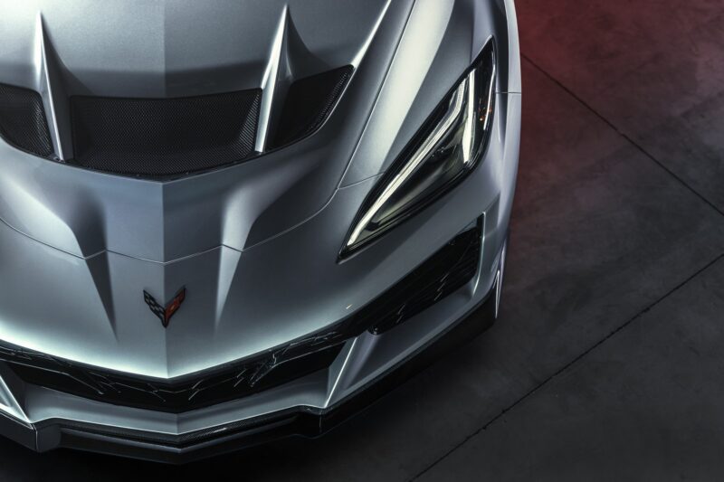 Close-up of the front end of a silver sports car with angular lines, prominent hood vents, and sharp LED headlights. Revealed: 2026 Corvette ZR1X is the most powerful Chevrolet ever built.