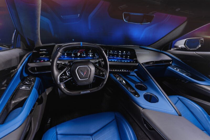The interior of a modern sports car, like the revealed 2026 Corvette ZR1X—the most powerful Chevrolet ever built—features a digital dashboard, flat-bottomed steering wheel, blue leather seats, illuminated controls, and touchscreens.