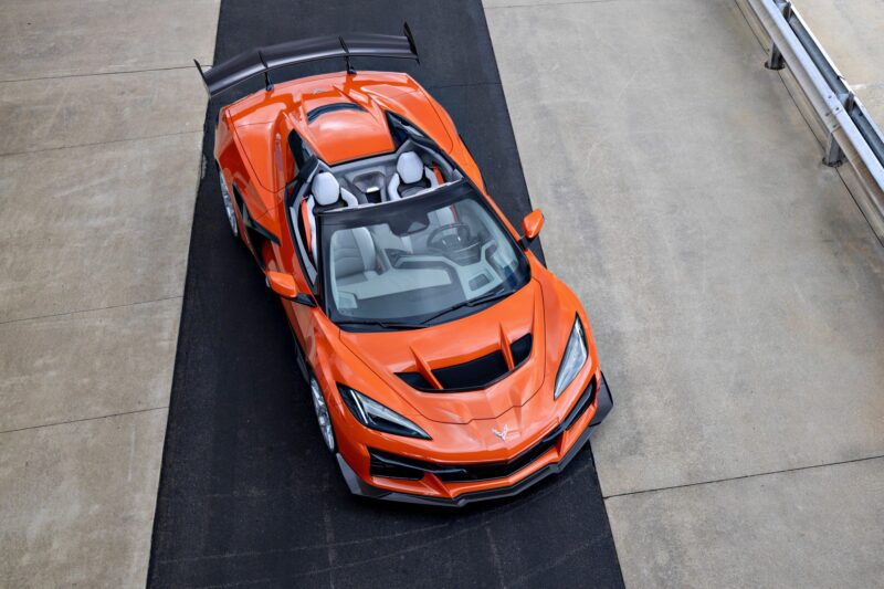 Top-down view of an orange Chevrolet Corvette ZR1X supercar with a large rear spoiler, parked on a black strip bordered by concrete.