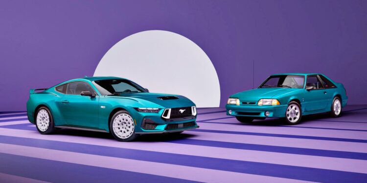 Two teal Ford Mustang cars, including a classic and a Fox-Body Mustang GT, are parked indoors on a striped purple floor with a large white semicircle backdrop.