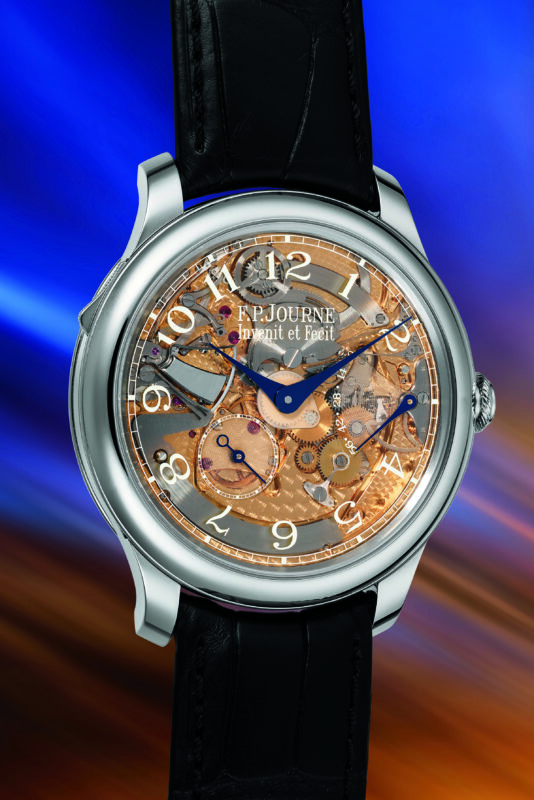 A luxury wristwatch with a transparent dial showing intricate gears and mechanisms, blue hands, Arabic numerals, and a black leather strap, showcased against a blurred blue and orange background at the Phillips New York Watch Auction.