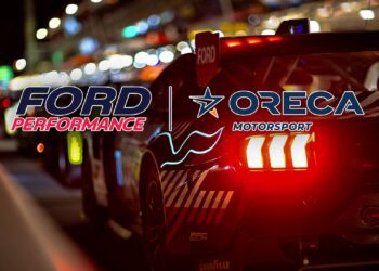 A race car with illuminated taillights is parked in a pit lane at night. The logos "Ford Performance" and "ORECA Motorsport" stand out, hinting at excitement for Ford returning to Le Mans and the anticipation of Ford Le Mans 2027.