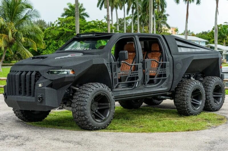 A large, black, six-wheeled off-road truck with open side doors and rugged tires is parked outdoors on a paved area with palm trees in the background—a unique creation for fans of custom cars for sale.