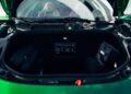 Open front trunk (frunk) of a green Ferrari 296 GTS, a modern tribute to performance, showing storage compartments with two black bags inside and interior details visible in the background.