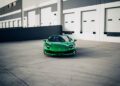 A green Ferrari 296 GTS is parked on concrete in front of a building with white garage doors and grey-striped walls—a modern tribute to Italian engineering, now for sale.