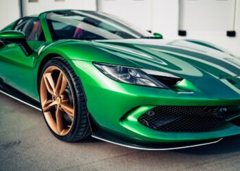 A close-up view of a shiny green Ferrari 296 GTS with gold wheels, a modern tribute parked on a concrete surface.