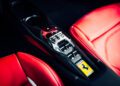 Close-up of a Ferrari 296 GTS central console with a metallic gear selector, black carbon fiber trim, and red leather seats with white stitching. The Ferrari logo offers a modern tribute to luxury—perfect for those seeking a Ferrari for sale.