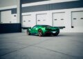 A green Ferrari 296 GTS with bronze wheels is parked in front of a modern industrial building with white garage doors—a striking modern tribute to Italian performance.
