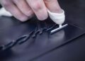 A gloved hand carefully applies a raised, black script emblem onto the glossy dark surface of a Porsche 911.