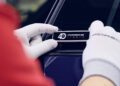 A person wearing white Porsche gloves affixes a "40 Porsche Targa" badge to a dark blue Porsche 911, highlighting the craftsmanship celebrated by Porsche Italia.