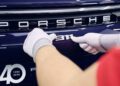 A person wearing white gloves applies the Porsche 911 badge to the rear of a car, with a "40" anniversary label visible below.