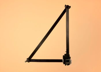 A black triangular metal frame with joints at each corner is displayed upright against a plain peach-colored background.