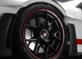 Close-up view of a black alloy wheel with red trim on a white Porsche 911 GT3 RS, featuring drilled disc brakes and part of the car's body with visible detailing at the Porsche Experience Center.