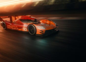 An orange Genesis race car with the number 10 drives on a track at sunset, blurred background indicating high speed.