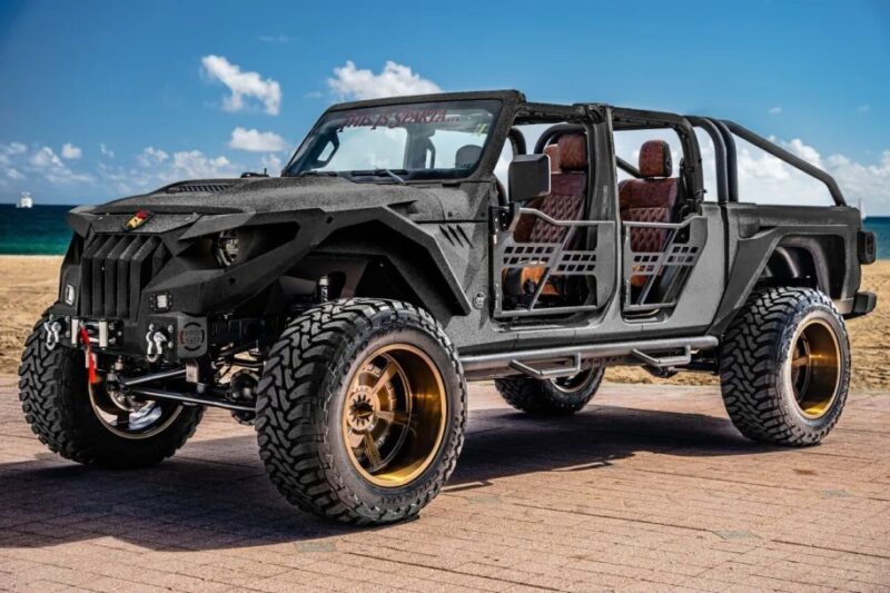 A heavily modified, black open-frame off-road vehicle with large tires and bronze rims—a unique creation parked on a paved surface near a beach—stands out as the ultimate find for enthusiasts searching for custom cars for sale.