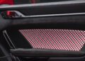 Close-up of a car door interior featuring a red and white checkered fabric panel, black trim, a metallic door handle, and a red fabric door pull in a 911 GT3 RS at the Porsche Experience Center.