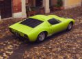 A Lamborghini in striking Verde Scandal sits parked on a cobblestone street in a courtyard, surrounded by arched doorways and potted plants.