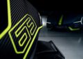 Close-up of a carbon fiber surface with a yellow "63" graphic; a Lamborghini in Verde Scandal with matching yellow accents is blurred in the background.