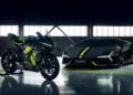 A Lamborghini sports car and a matching motorcycle in striking black and Verde Scandal neon yellow are parked side by side in a dimly lit garage with large windows.