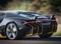 Close-up of the rear of a black Lamborghini Few-Off sports car with yellow accents driving on a road, showcasing its taillights, spoiler, and exhaust system during Monterey Car Week.