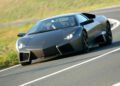 A matte black Lamborghini Few-Off speeds along a winding road, surrounded by lush greenery—a rare sight reminiscent of Monterey Car Week exclusivity.
