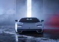 A Few-Off white Lamborghini sports car is parked indoors on a wet concrete floor, facing the camera with its headlights on—an exclusive sight often seen at Monterey Car Week.