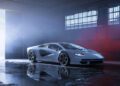 A silver Lamborghini Few-Off sports car is parked in a dimly lit garage with large windows and a partially open door letting in natural light, reminiscent of scenes from Monterey Car Week.