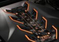 Close-up of a car engine cover with "Mansory P850 Performance" branding, featuring black and orange accents and a carbon fiber design.