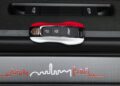 A Porsche key fob rests on a carbon fiber surface featuring a red and white line graphic of a city skyline, reminiscent of the dynamic energy at the Porsche Experience Center Toronto.