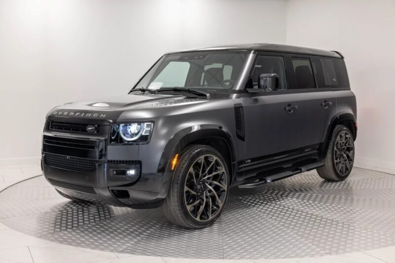 The Land Rover Defender Black SUV stops with custom wheels, black trim, and a brand in a well-lit white display-which creates a unique garage for custom car fans.