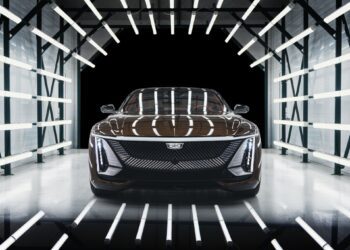A black Cadillac electric car is positioned under bright, parallel LED lights in a tunnel-like setting, facing the camera directly.