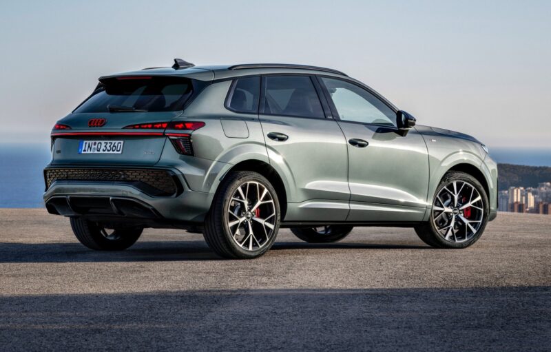 A grey 2026 Audi Q3 breaks cover, parked on an open surface with a city and ocean visible in the background—showcasing what's new in its striking design.