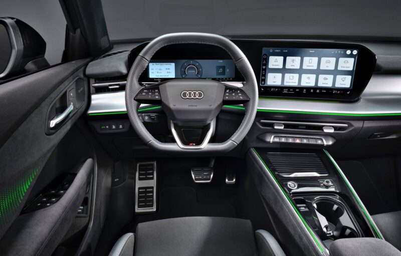 Interior view of the 2026 Audi Q3 breaks cover, showcasing the steering wheel, digital instrument cluster, widescreen infotainment display, and ambient green lighting accents.