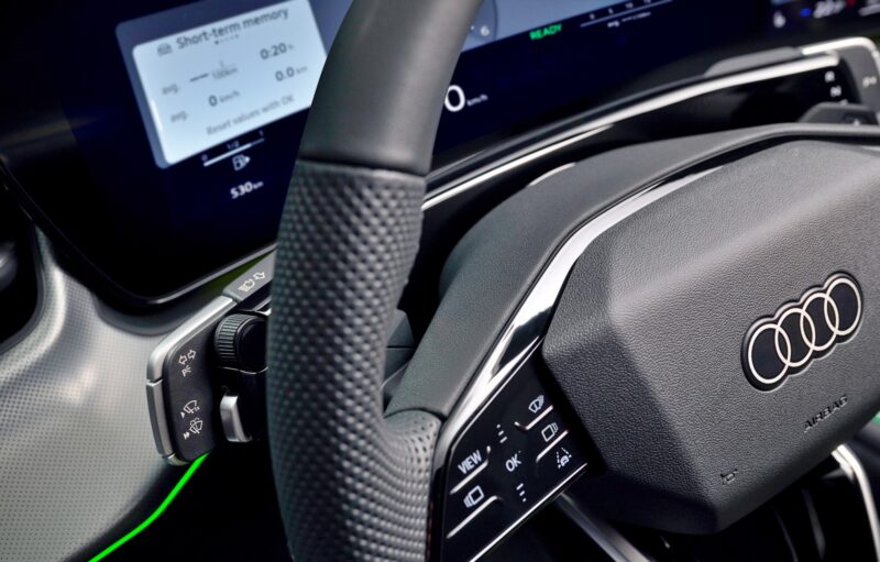 Close-up of the 2026 Audi Q3 steering wheel, showcasing dashboard controls, buttons, and part of the digital instrument display in the background—highlighting what's new in this latest model.