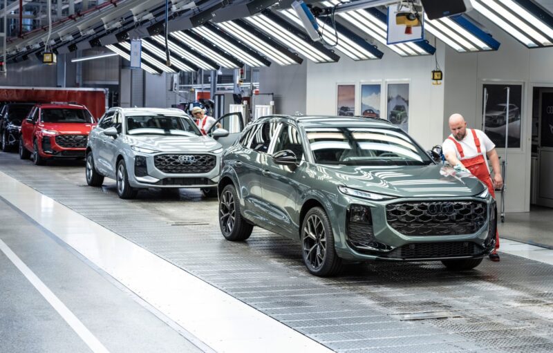 Workers inspect and finish new SUVs, including the 2026 Audi Q3 Breaks Cover: Here’s What’s New, on an assembly line in a modern automotive factory under bright overhead lights.