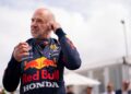 A man in a Red Bull Honda racing suit adjusts his earpiece outdoors during the Festival of Speed, with people and a building visible in the blurred background.