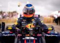 A Formula 1 driver in full racing gear and helmet sits in a Red Bull car on a track, facing forward, with blurred spectators in the background—capturing the excitement of 75 Years of F1 at the Festival of Speed.