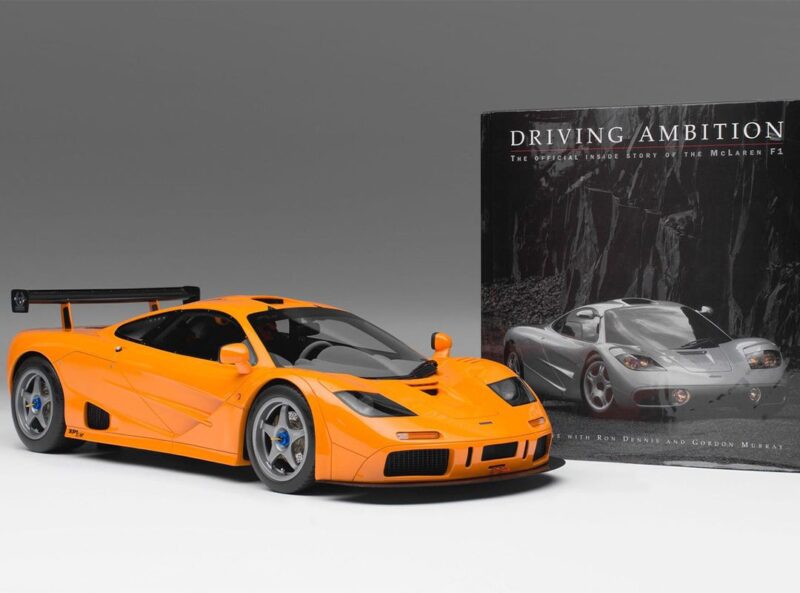 An orange McLaren F1 model car is displayed in front of "Driving Ambition: The Official Inside Story of the McLaren F1," making it a standout pick for any Father's Day Gift Guide featured by duPont REGISTRY.