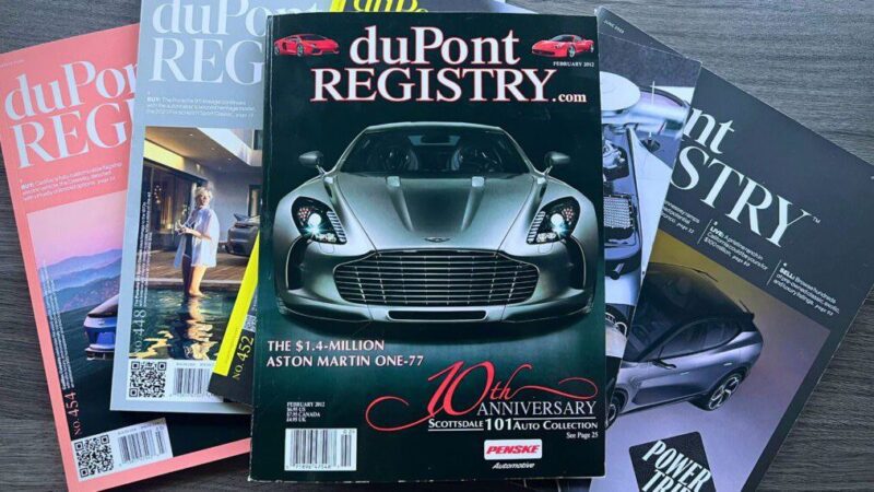 Four issues of duPont REGISTRY magazine are stacked, with the top featuring The Incredible Story Of The '78th' Aston Martin One-77, plus highlights on the 10th anniversary and exclusive luxury car content.