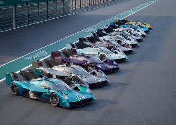 A row of Aston Martin race cars, including the limited to 10, track-only Valkyrie LM with Le Mans DNA, are lined up side by side on a racetrack pit lane.