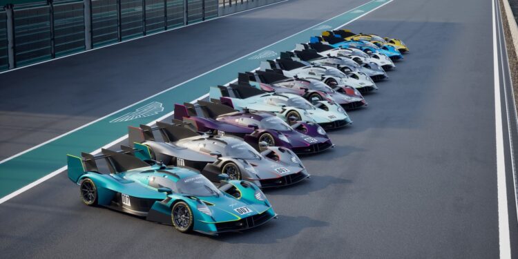 A row of Aston Martin race cars, including the limited to 10, track-only Valkyrie LM with Le Mans DNA, are lined up side by side on a racetrack pit lane.