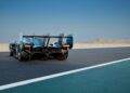 A futuristic race car with prominent rear fins and lights is parked on an empty racetrack, with mountains visible in the background—this is the track-only Valkyrie LM, Aston Martin’s latest hypercar with Le Mans DNA.