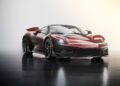 A sleek, red Pininfarina Battista with black accents is parked on a glossy surface in a brightly lit studio setting.