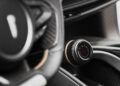 Close-up of a Pininfarina Battista steering wheel and a control knob with a red power symbol and adjustment levels on the dashboard.