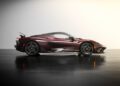 A maroon Pininfarina Battista luxury sports car is parked indoors on a polished black floor, viewed from the side against a light gradient background.