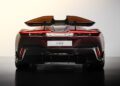 Rear view of a sleek, modern Pininfarina Battista sports car with prominent taillights, a large rear wing, and a dark red and black color scheme against a plain background.