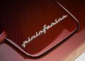 Close-up of a metallic "pininfarina" emblem on a glossy red carbon fiber panel of the Last Battista.