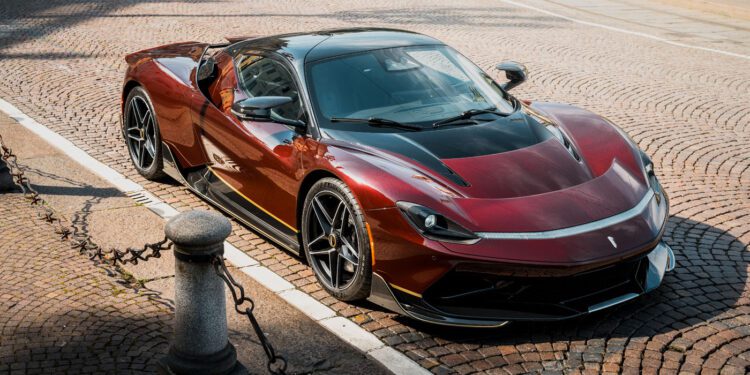 A sleek red and black Pininfarina Battista sports car is parked on a cobblestone street near a curb lined with short metal posts and chains.
