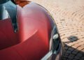 Close-up of a Pininfarina Battista hood with a visible headlight, carbon fiber detailing, and brick pavement in the background.