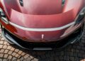 A close-up view of the front of a red Pininfarina Battista with a carbon fiber hood, parked on a cobblestone surface.